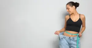 A woman happily holding up her loose-fitting jeans after medical weight loss in Orlando, FL